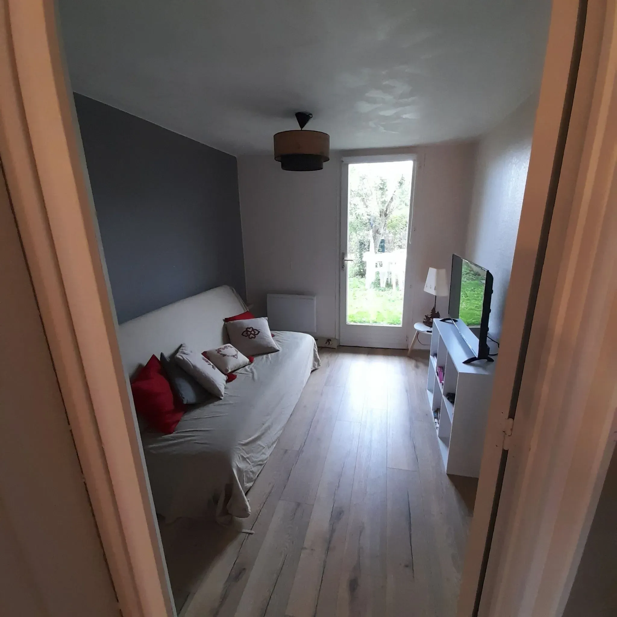 Salon avec canapé, télévision et porte-fenêtre sur le jardin