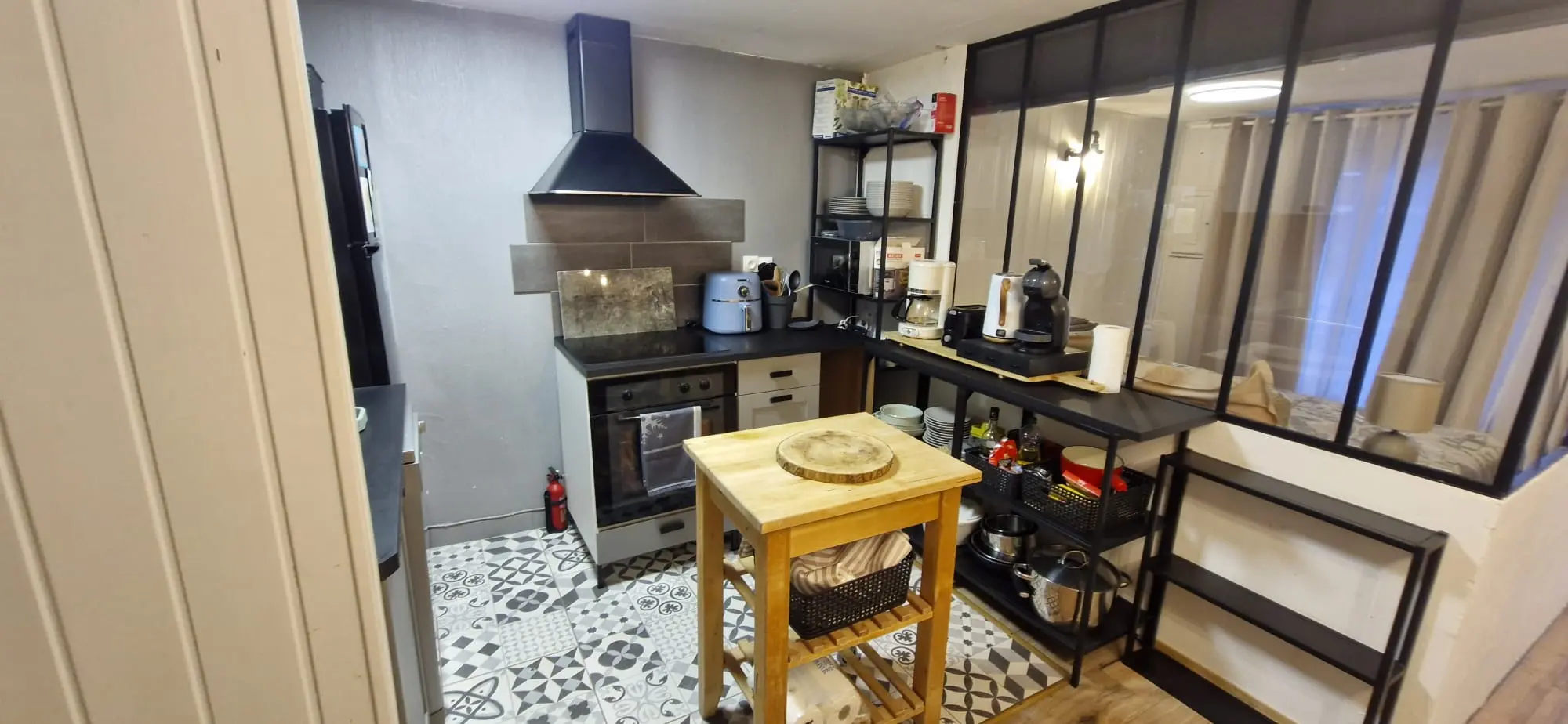 Cuisine avec îlot en bois, plaque de cuisson et verrière sur le séjour
