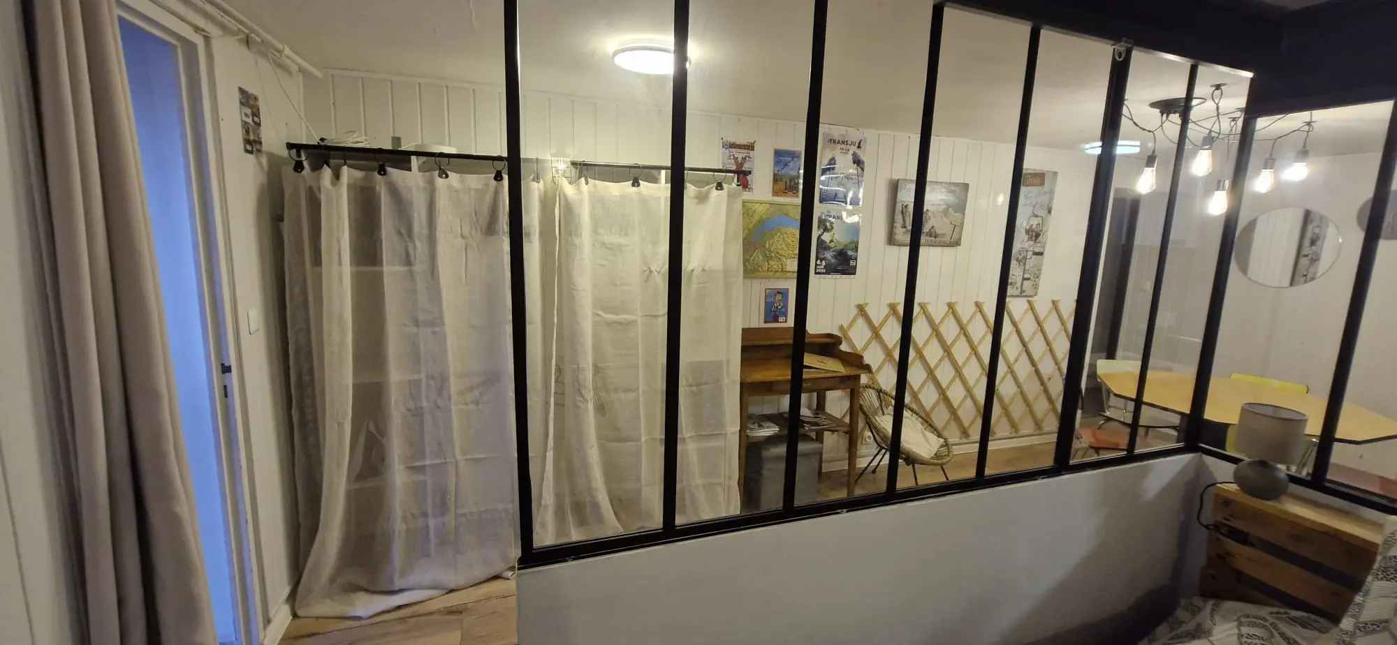 Verrière noire et rideaux de lin, avec le coin bureau et la salle à manger derrière